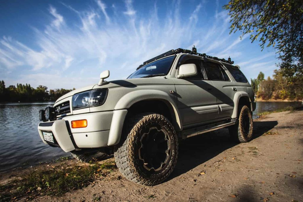 White Toyota Hilux Surf 4x4 parked on a lakeside track, modified for off-road use and imported from Japan.